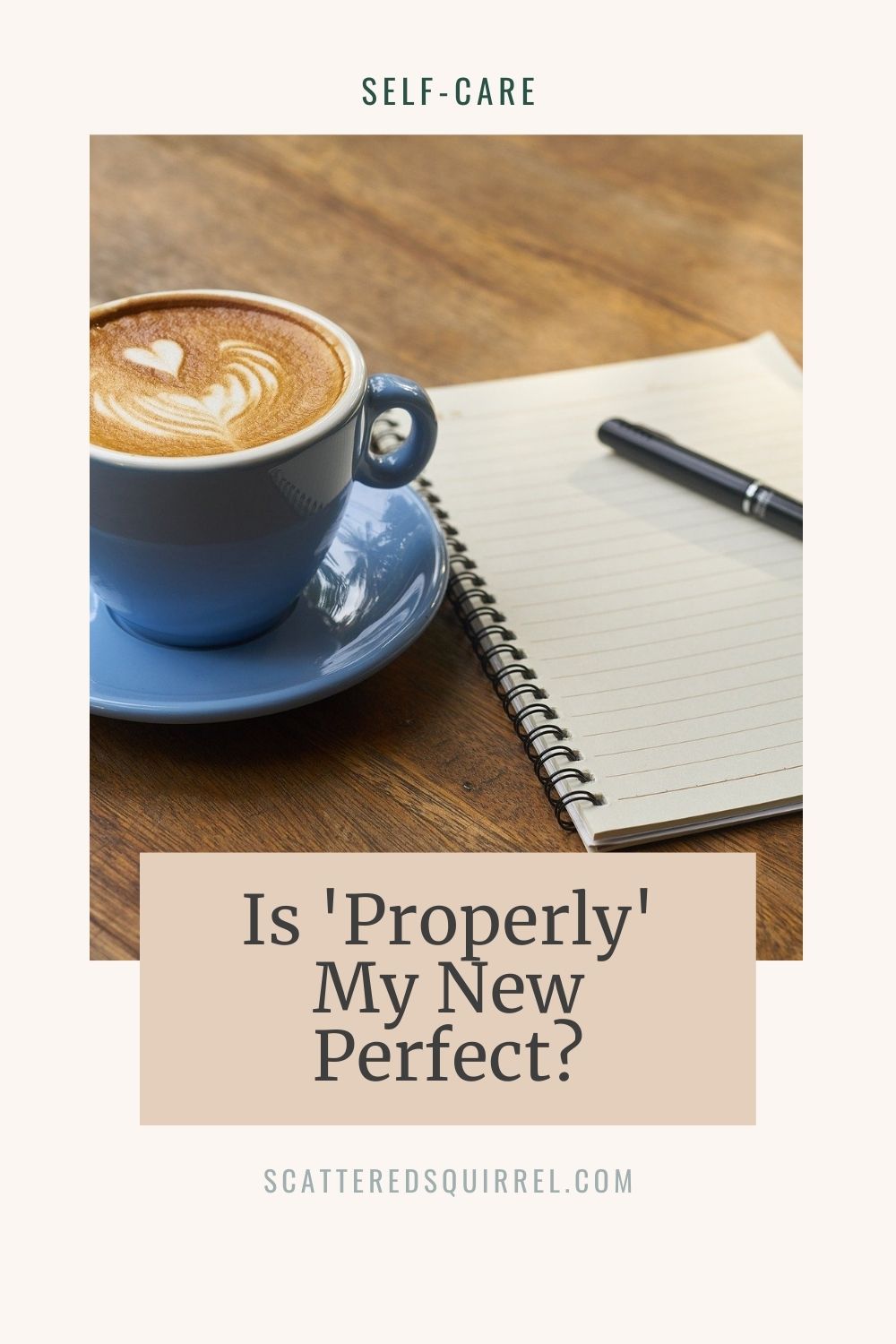 small blue cup of capicino with heart in the foam, on a matching blue saucer. To the right of the cup is a spiral bound notebook with a pen on top.