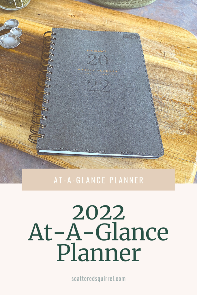 A closed, wire-o bound planner is sitting on a cutting board. The cober is a grey faux suede and it readys At-A-Glance Weekly Planner Tow Thousand-Twety Two in copper text with 2022 blind embossed between the lines of text.