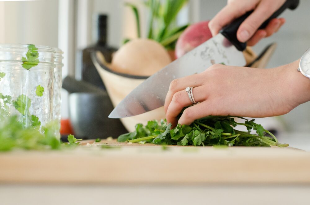 A woman wearing a wedding band set is chopping parsley on a wooden cutting board.