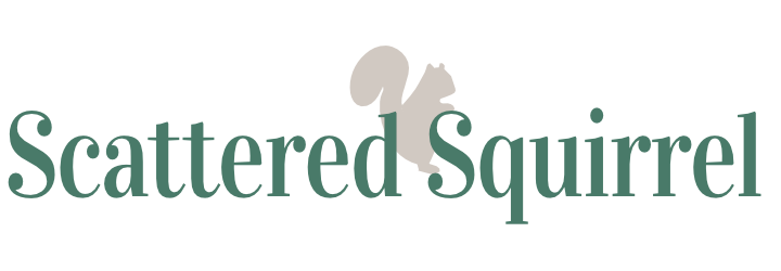This image is the website logo for scattered squirrel dot com. The name "Scattered Squirrel" is written in a green, serif font. Standing on the second 'S' just behind the 'D' is a grey silhouette of a squirrel.